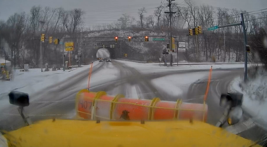 The front of a PennDOT plow truck from the operator's perspective looking over a snow-covered intersection.